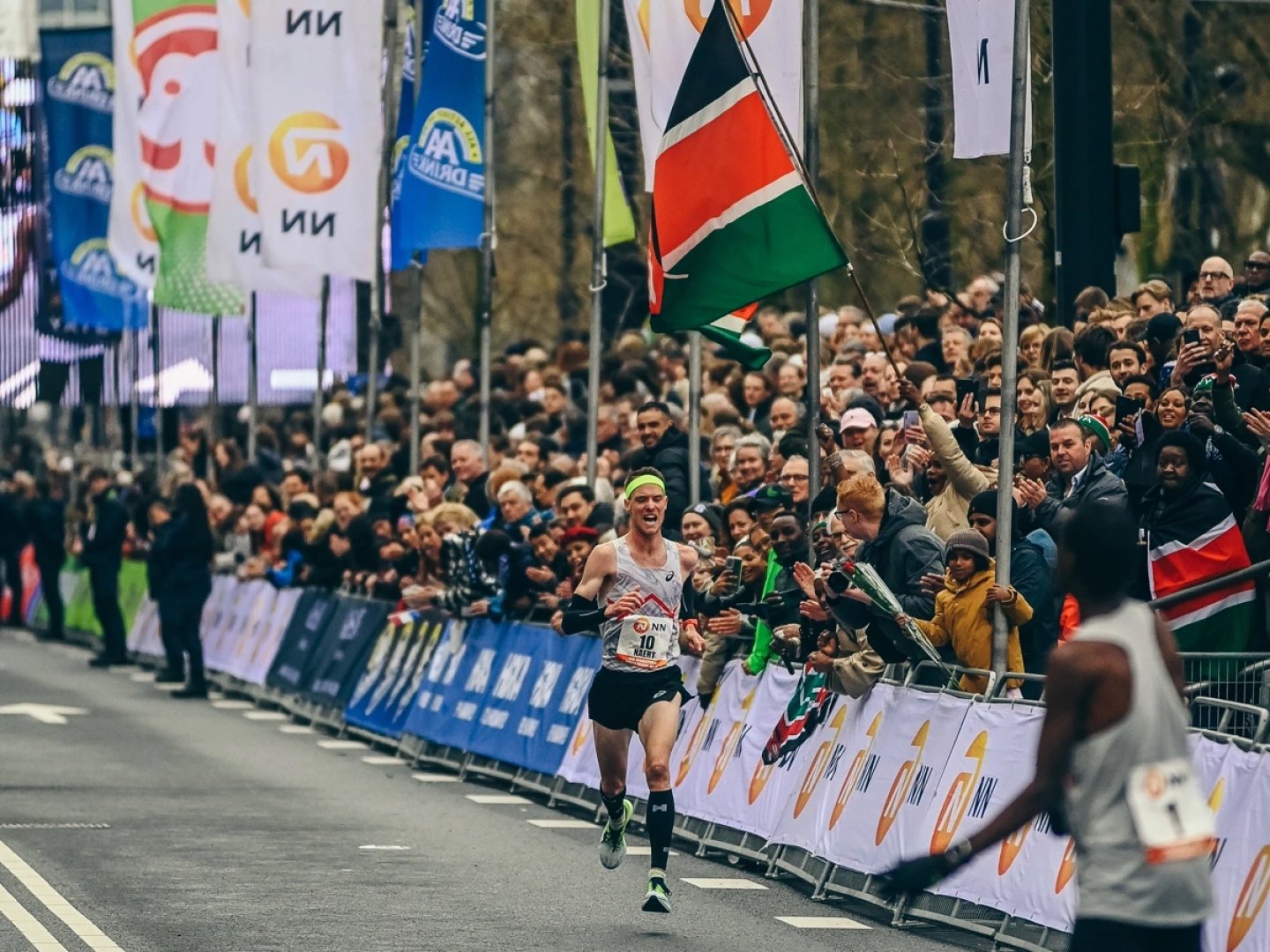 Elite male runner bib number 10 in ASICS singlet sprinting past cheering spectators at Rotterdam Marathon