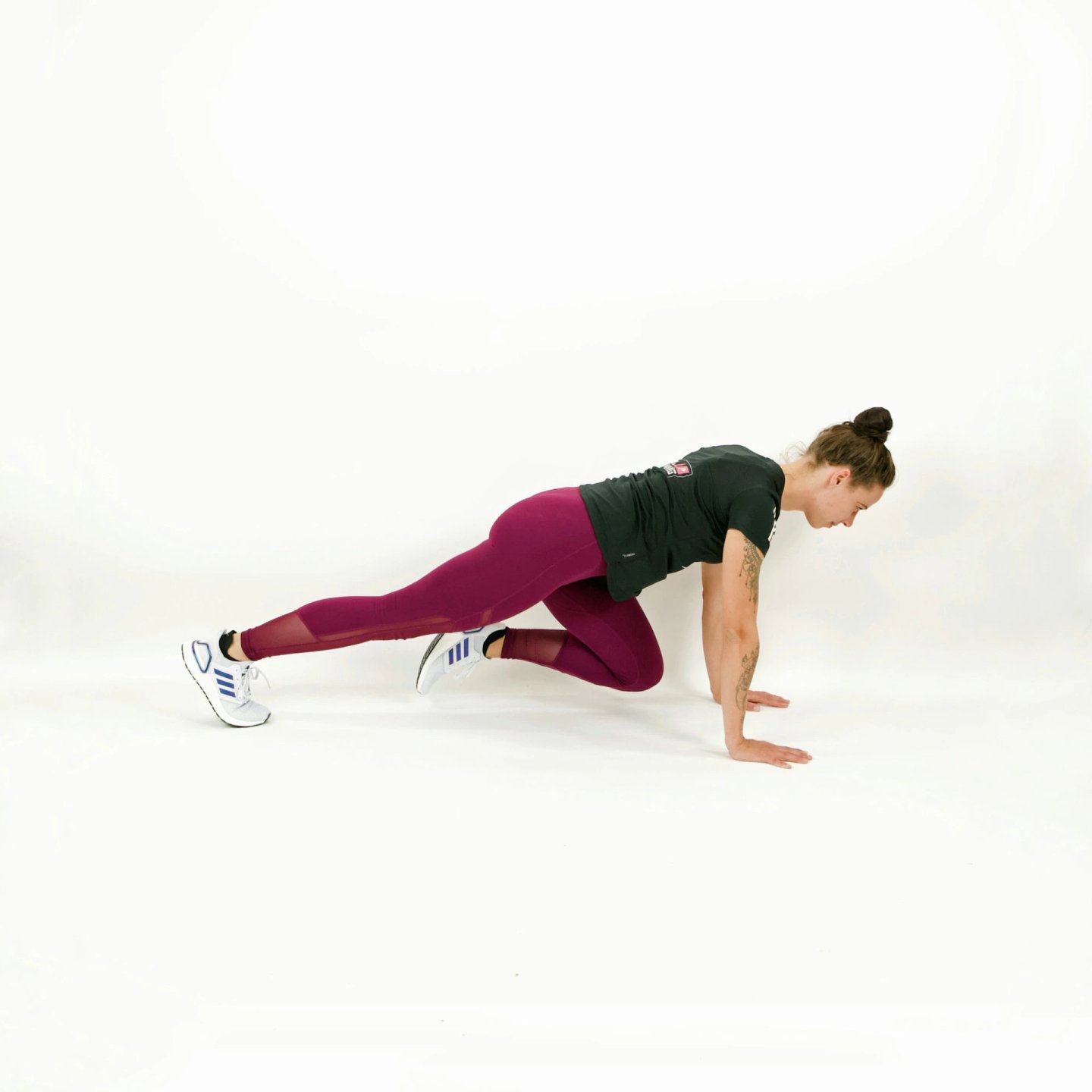 Woman in burgundy leggings and white Adidas trainers performing mountain climber exercise in a plank position