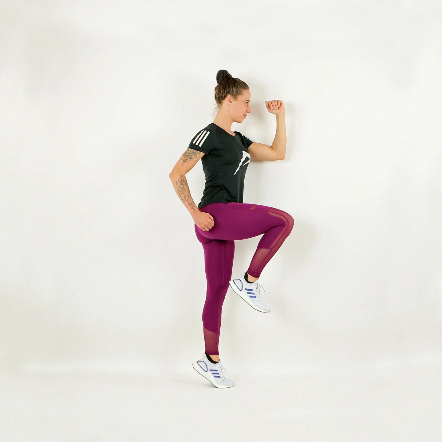 Woman in purple leggings and black Adidas t-shirt performing high-knee running drill on white background