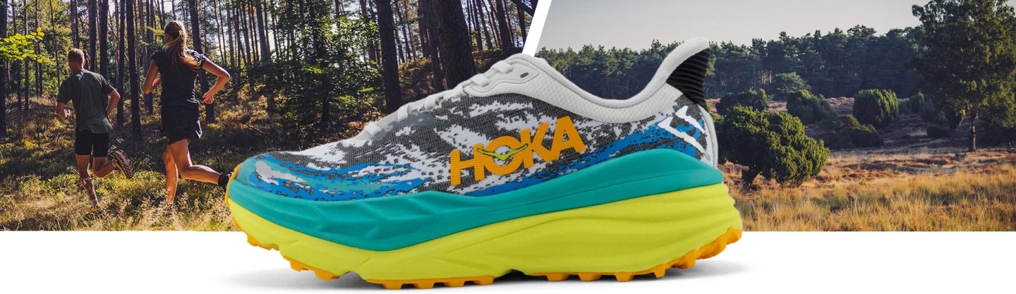 Hoka Stinson ATR 7 trail running shoe in white, teal and yellow colourway, shown against a forest trail backdrop