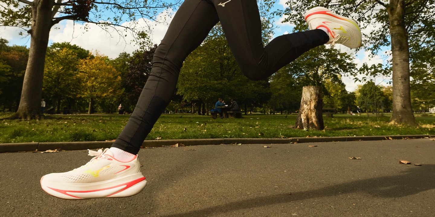 Close-up of a runner's legs in Mizuno Sky Prime shoes with coral and yellow accents running on a park path.
