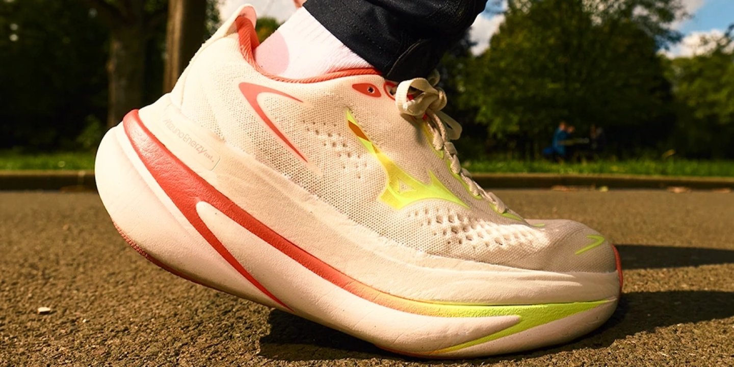 Mizuno Sky Prime running shoe in white with coral and neon yellow accents, worn outdoors on tarmac in a park setting.