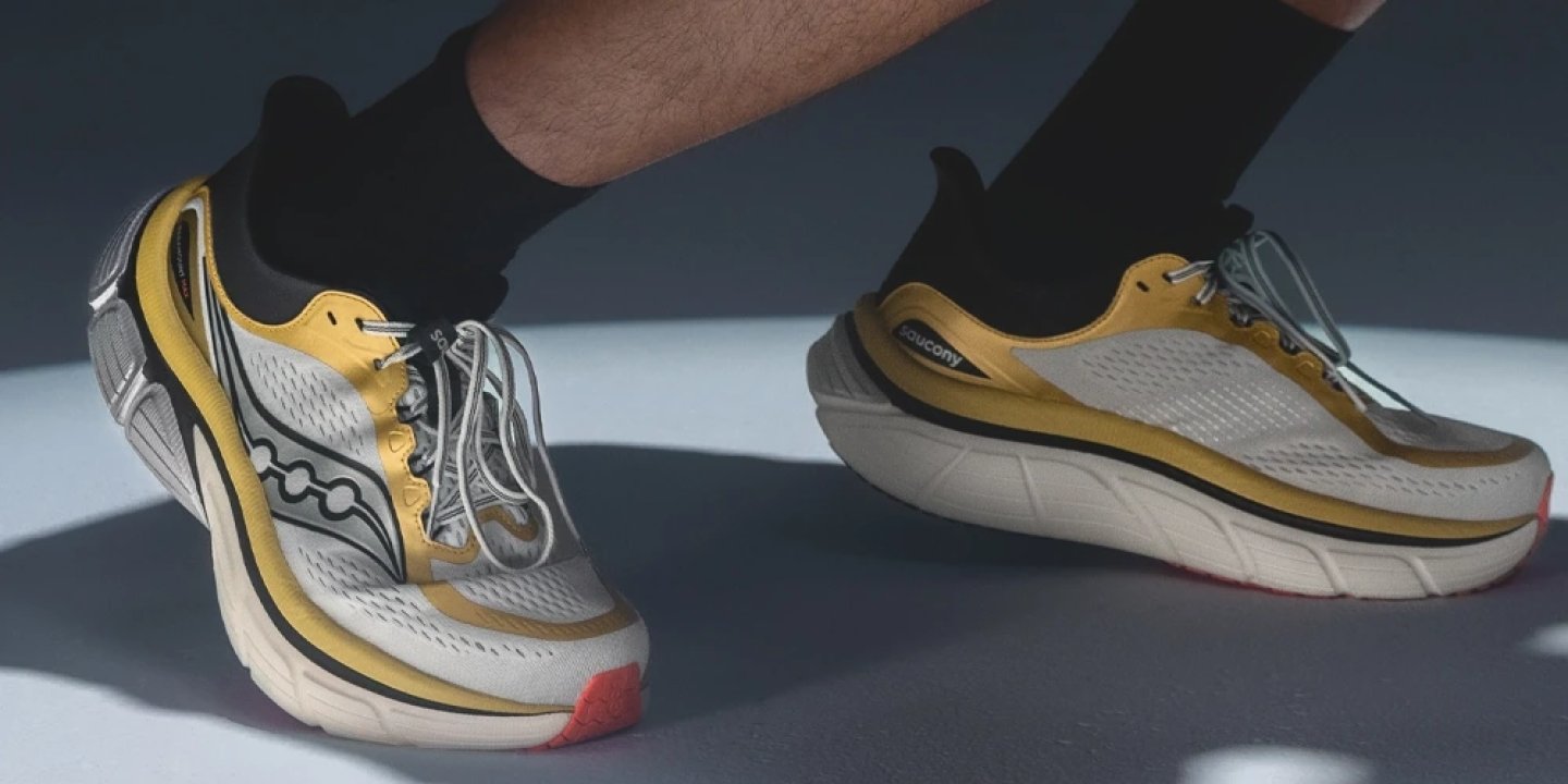 Close-up of Saucony Paramount Max running shoes in yellow and white on feet with black socks, showcasing thick midsole cushioning.