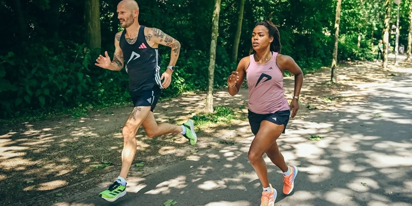 Man and woman running side by side on a shaded park path wearing adidas running apparel and racing shoes