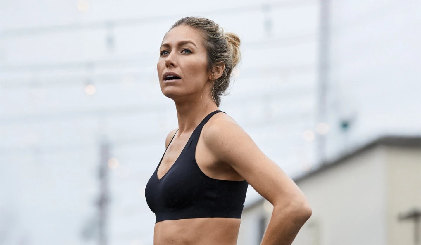 Woman wearing the Brooks Run Bra 11 in black, shown outdoors mid-run in a cropped athletic bra top.