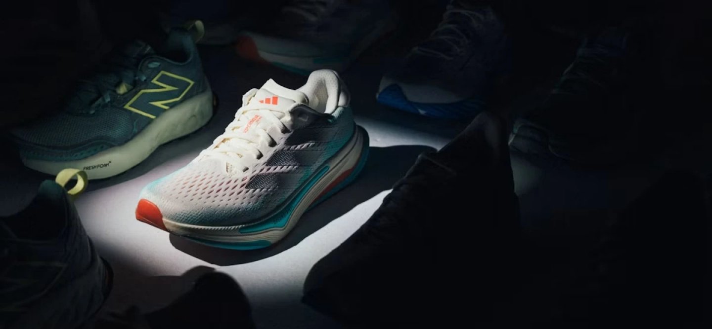 Adidas running shoe in white, teal and coral colorway illuminated under spotlight surrounded by other running shoes