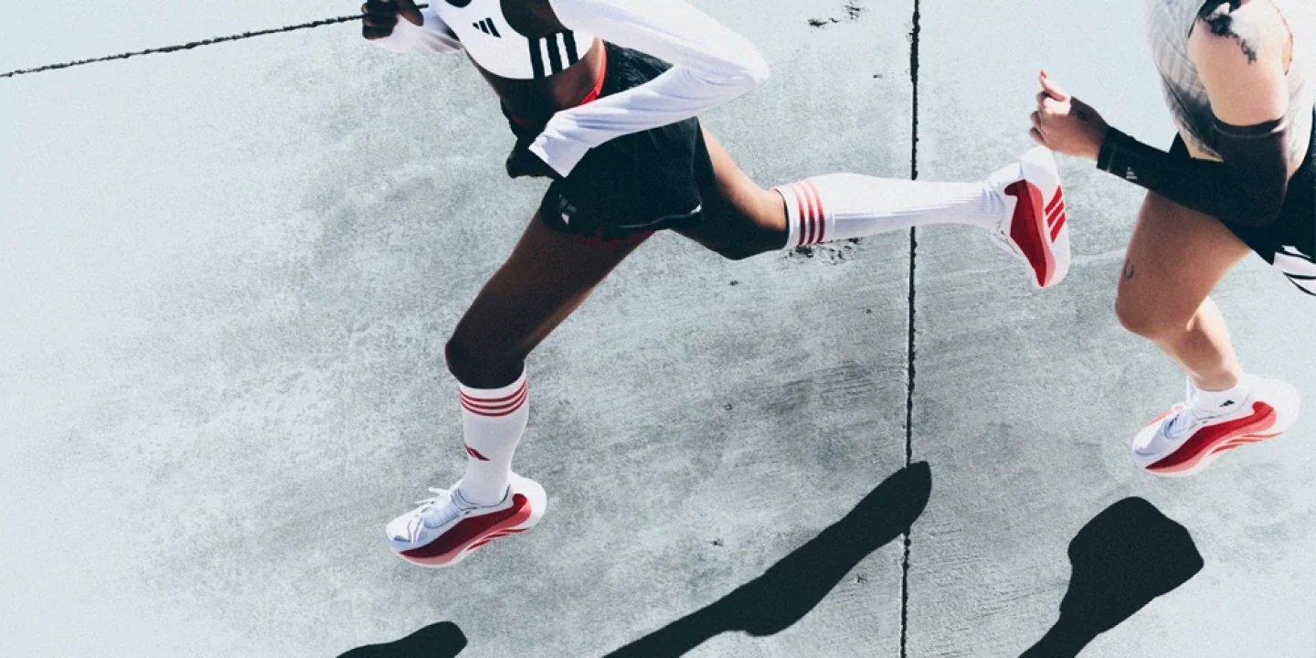 Two women running on concrete wearing white and red adidas running shoes with knee-high striped socks.