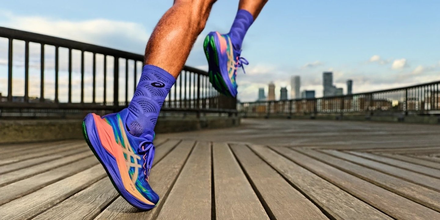 Close-up of ASICS running shoes in purple and coral colourway with matching socks, runner mid-stride on wooden boardwalk