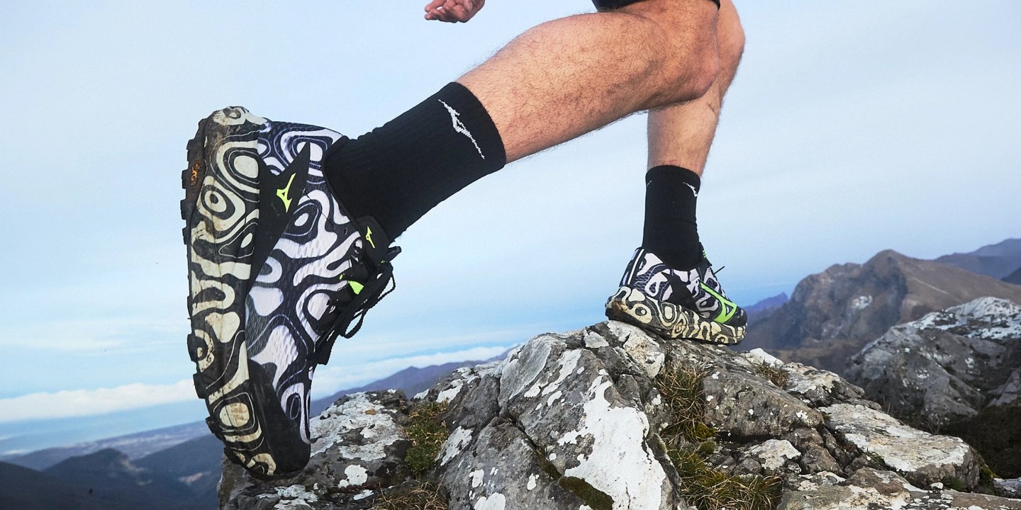 Male trail runner wearing Mizuno trail shoes with bold black and white swirl pattern and neon accents.