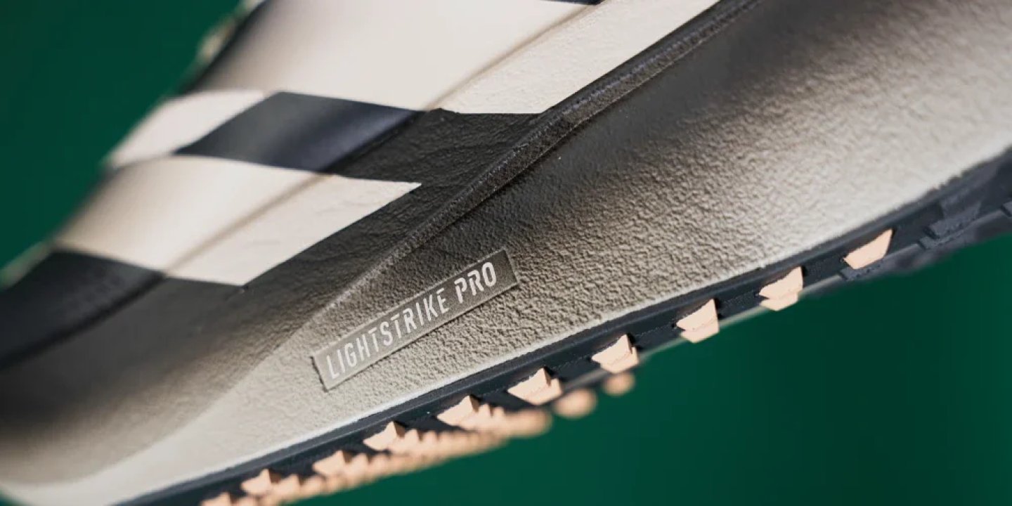 Close-up of Adidas running shoe midsole showing embossed Lightstrike Pro label with three stripes and rubber outsole lugs.