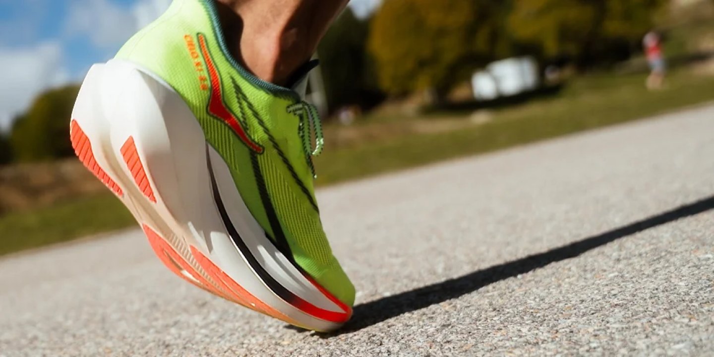 Close-up of a neon green and orange carbon plate running shoe on a road surface during an outdoor run.