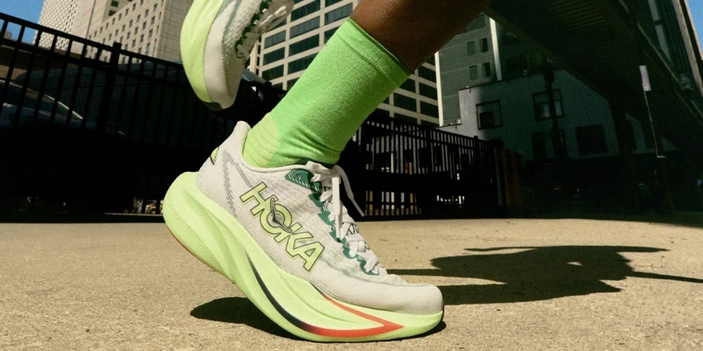 Runner wearing a white and neon green HOKA running shoe with lime green crew socks on a city street.