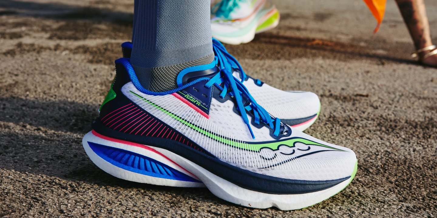 Side profile of Saucony Endorphin Shift running shoe in white, navy, green and pink on a road surface