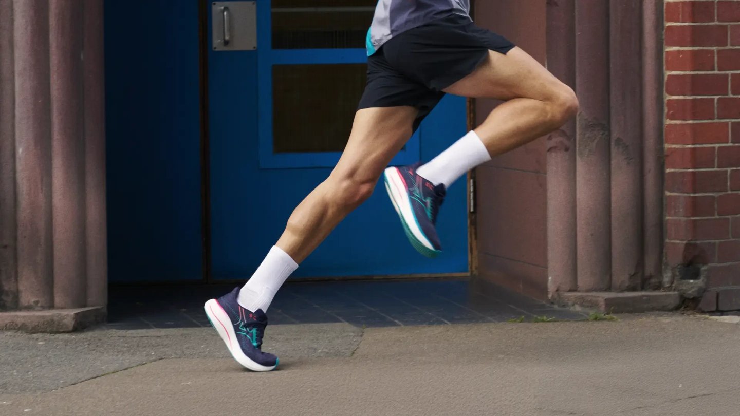 Male runner mid-stride wearing Mizuno Wave Rider 27 in navy, teal and pink colorway on urban pavement