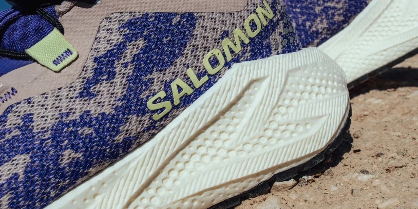 Close-up of Salomon trail running shoe showing white foam midsole texture and blue speckled knit upper with lime logo.