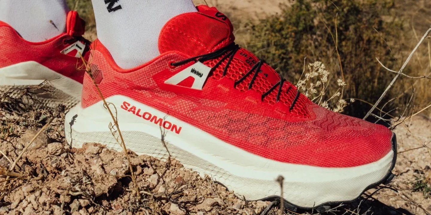 Salomon Ultra Glide red trail running shoe with white midsole worn on rocky ground outdoors.
