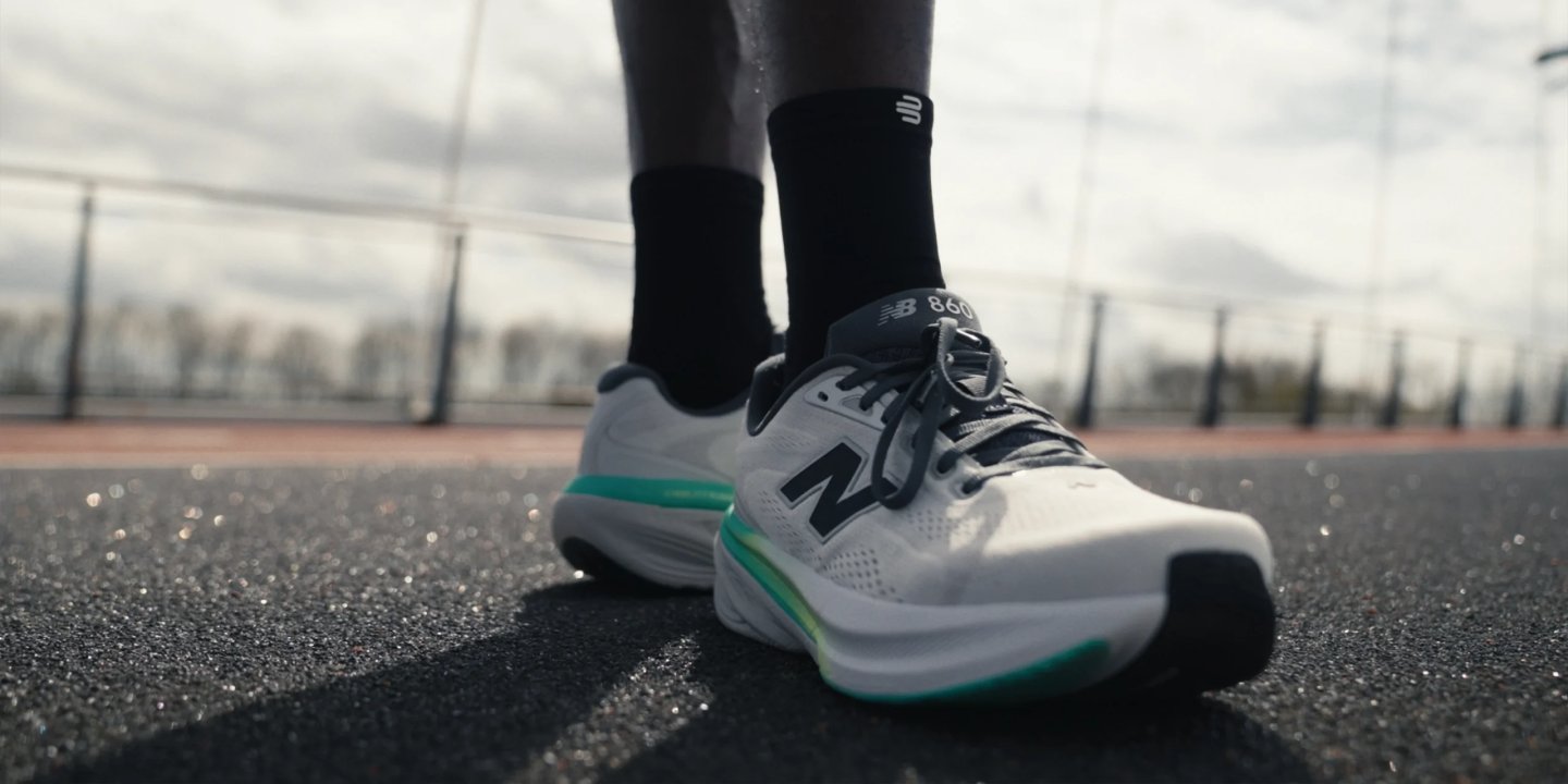 New Balance 860 white and teal stability running shoe worn on a wet outdoor running track.