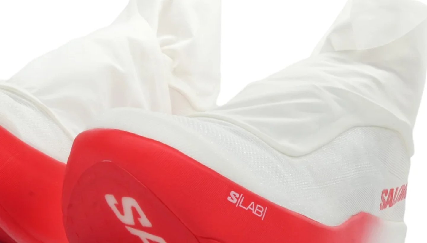 Salomon S/LAB running shoe with white knit upper and red midsole, showing S/LAB and Salomon branding.