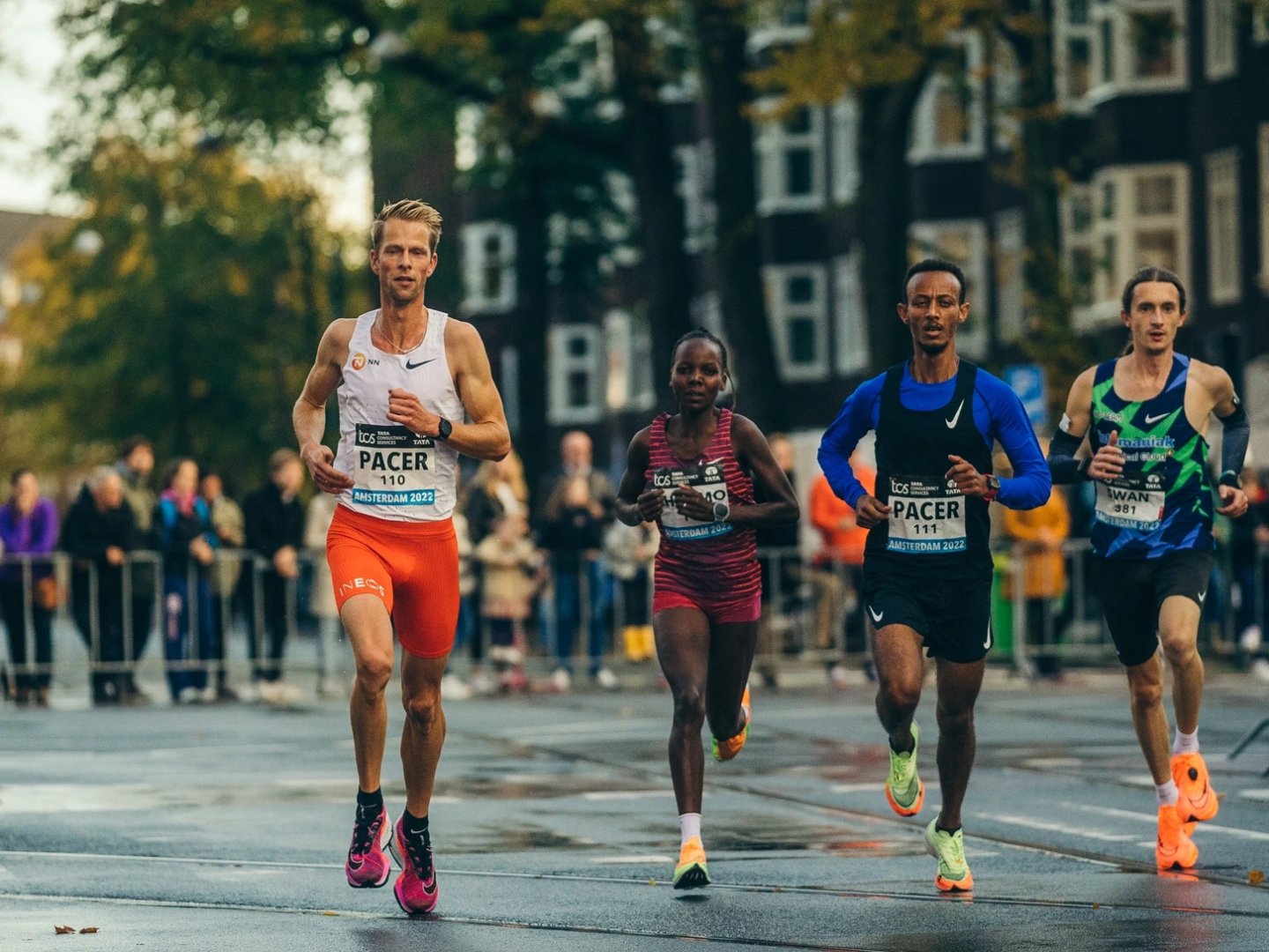 Four runners including two pacers numbered 110 and 111 racing through wet Amsterdam streets at the 2022 TCS Amsterdam Marathon.