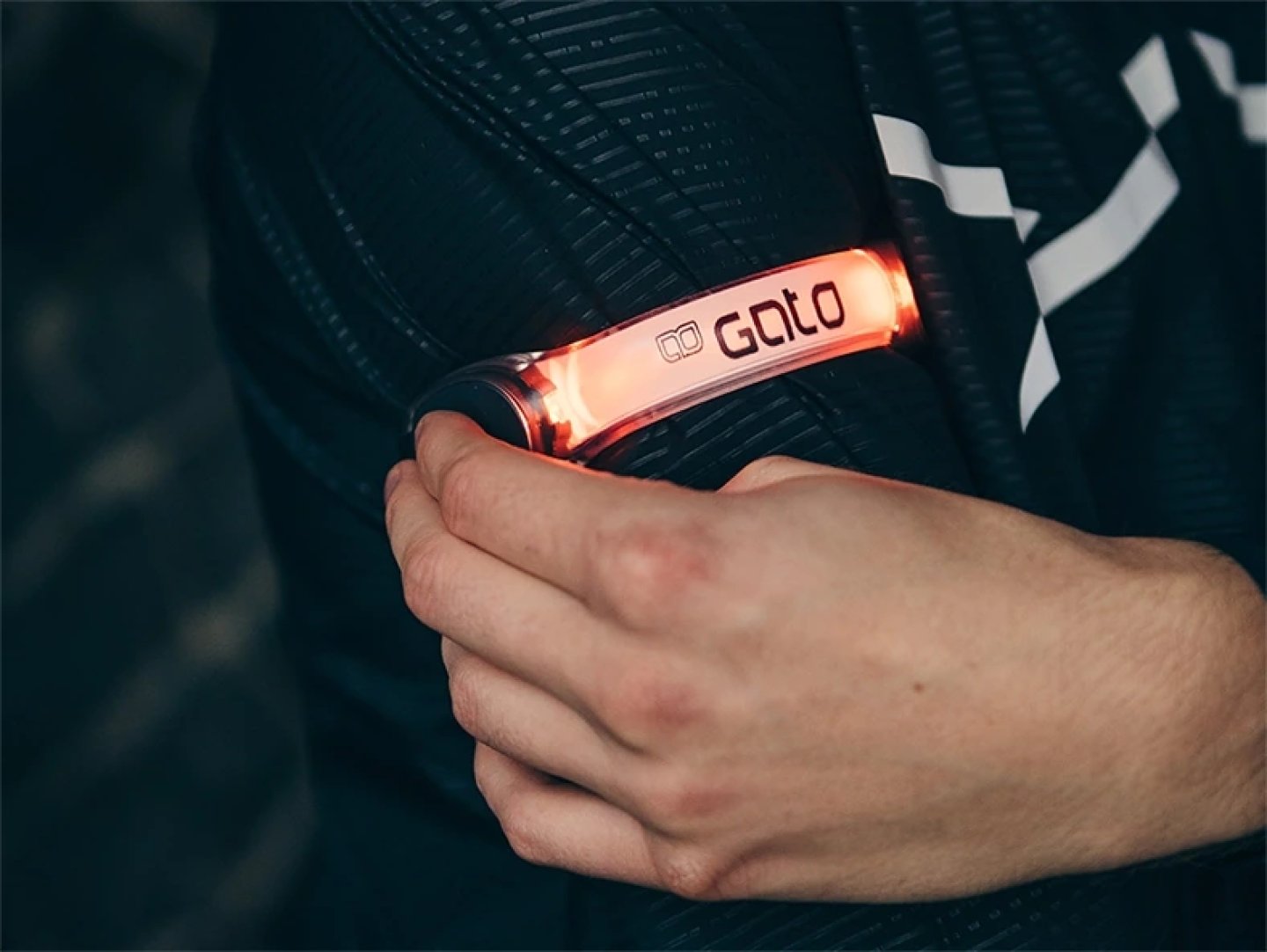 Gato branded red LED clip safety light attached to a black running jacket shoulder strap, glowing brightly.