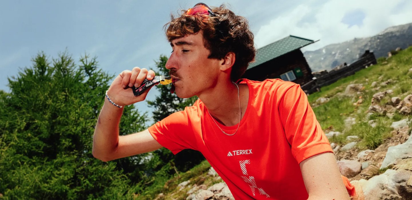 Trail runner in an orange shirt taking an energy gel in the mountains