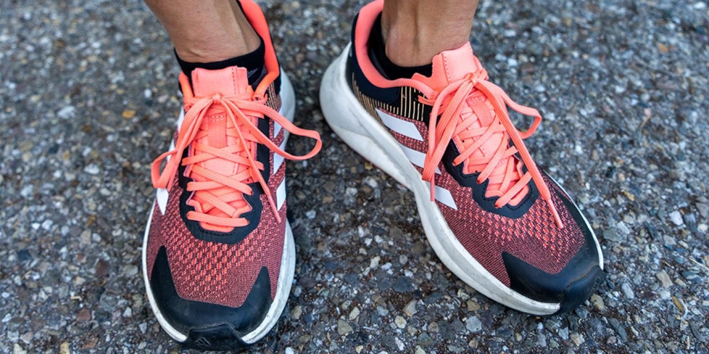 Adidas Soulstride running shoes in coral and black knit upper with white Boost midsole, worn on tarmac surface