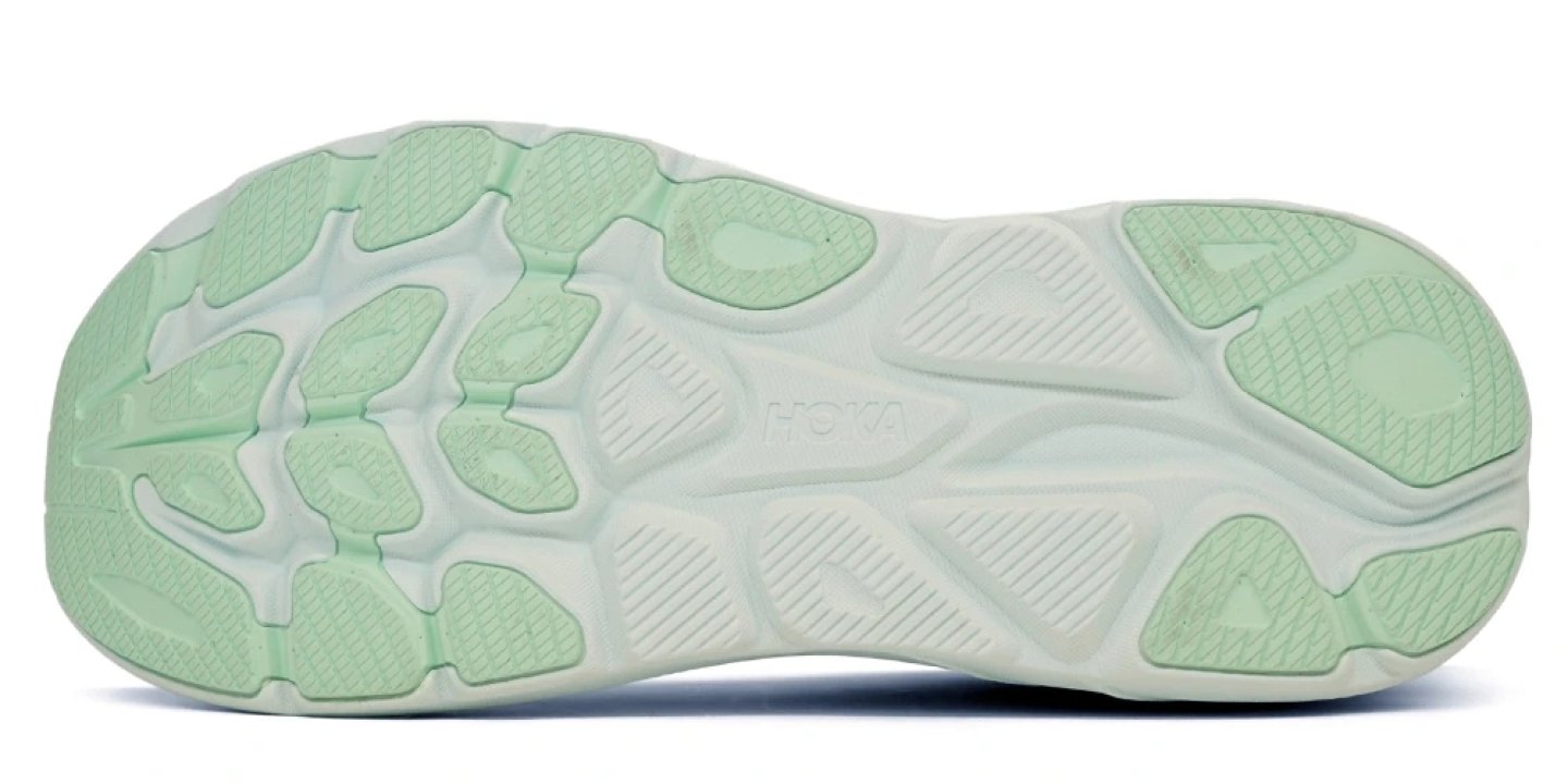 Bottom view of a Hoka running shoe outsole in mint green, showing segmented rubber lugs and rocker-shaped profile
