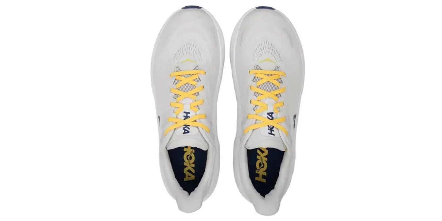 Top view of HOKA running shoes in white with yellow laces and navy blue branded insoles.