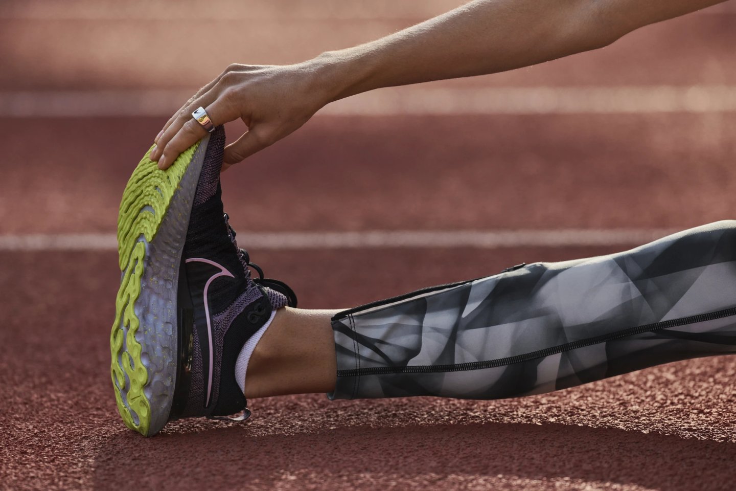Close-up of a runner stretching on a red athletics track wearing black Nike running shoes with a bright green outsole