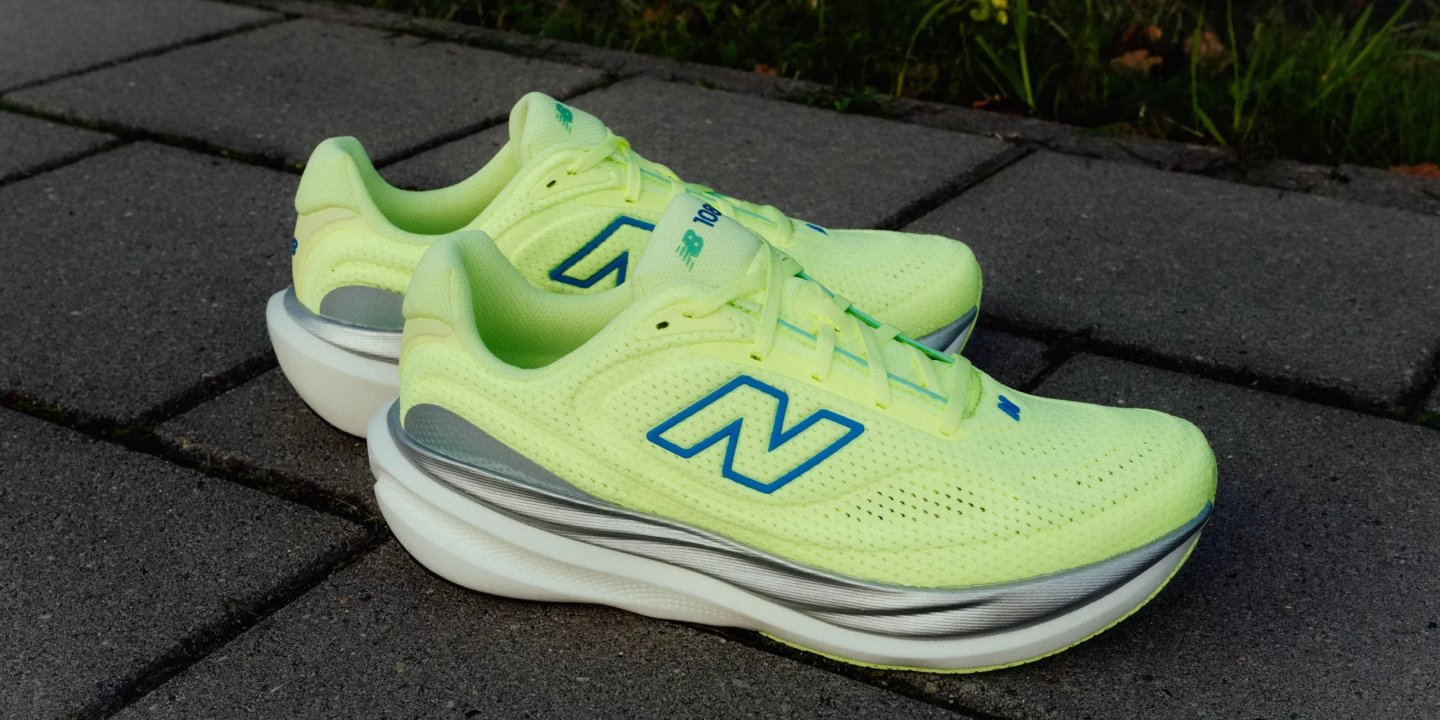 New Balance SuperComp Trainer V2 running shoes in lime yellow with blue N logo and stacked carbon-plate midsole on paving.