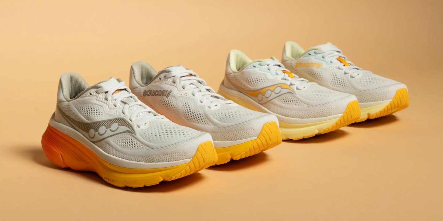 Three Saucony running shoes in white with yellow and orange outsoles displayed side by side on a beige background