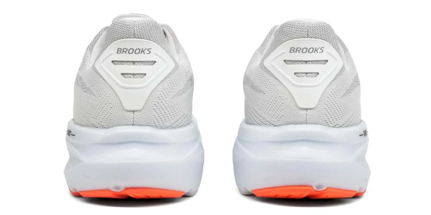 Rear view of a pair of Brooks Ghost 17 running shoes in white and grey with an orange outsole