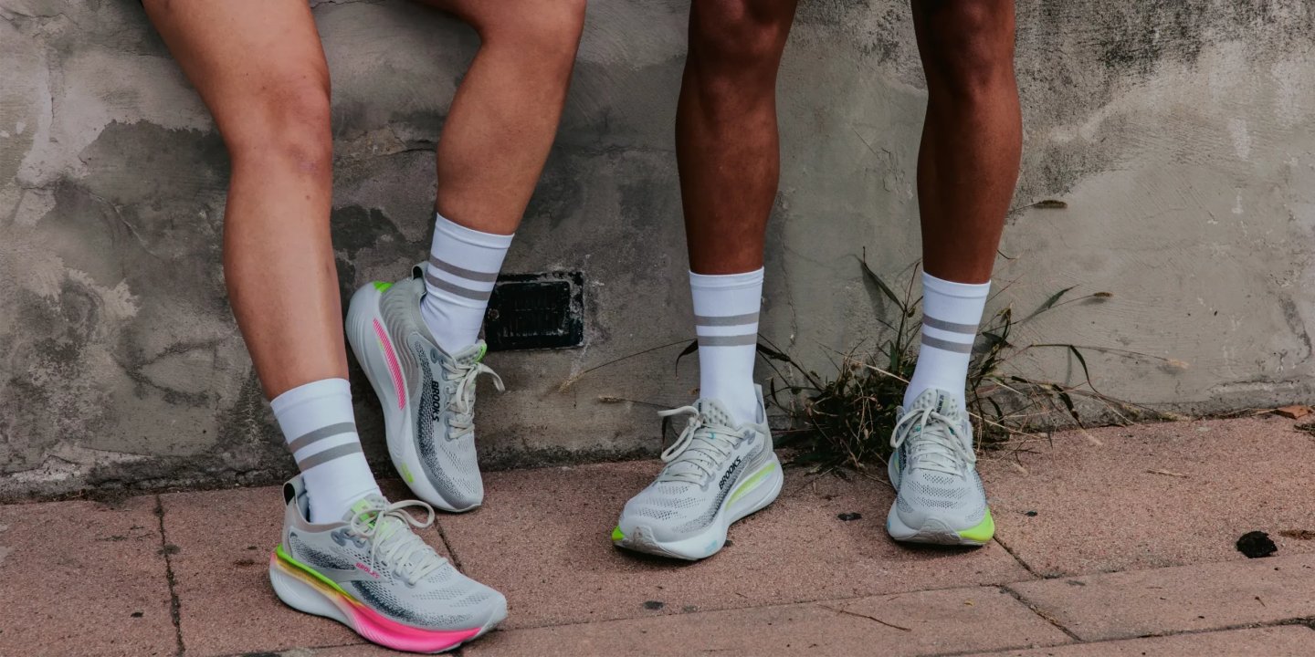 Two runners wearing Brooks Hyperion Max running shoes in light grey with neon yellow and pink accents.