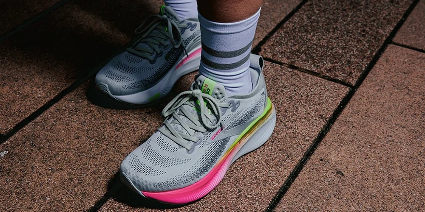 Close-up of Brooks Hyperion Max running shoes in grey with pink and neon yellow gradient midsole on brick pavement