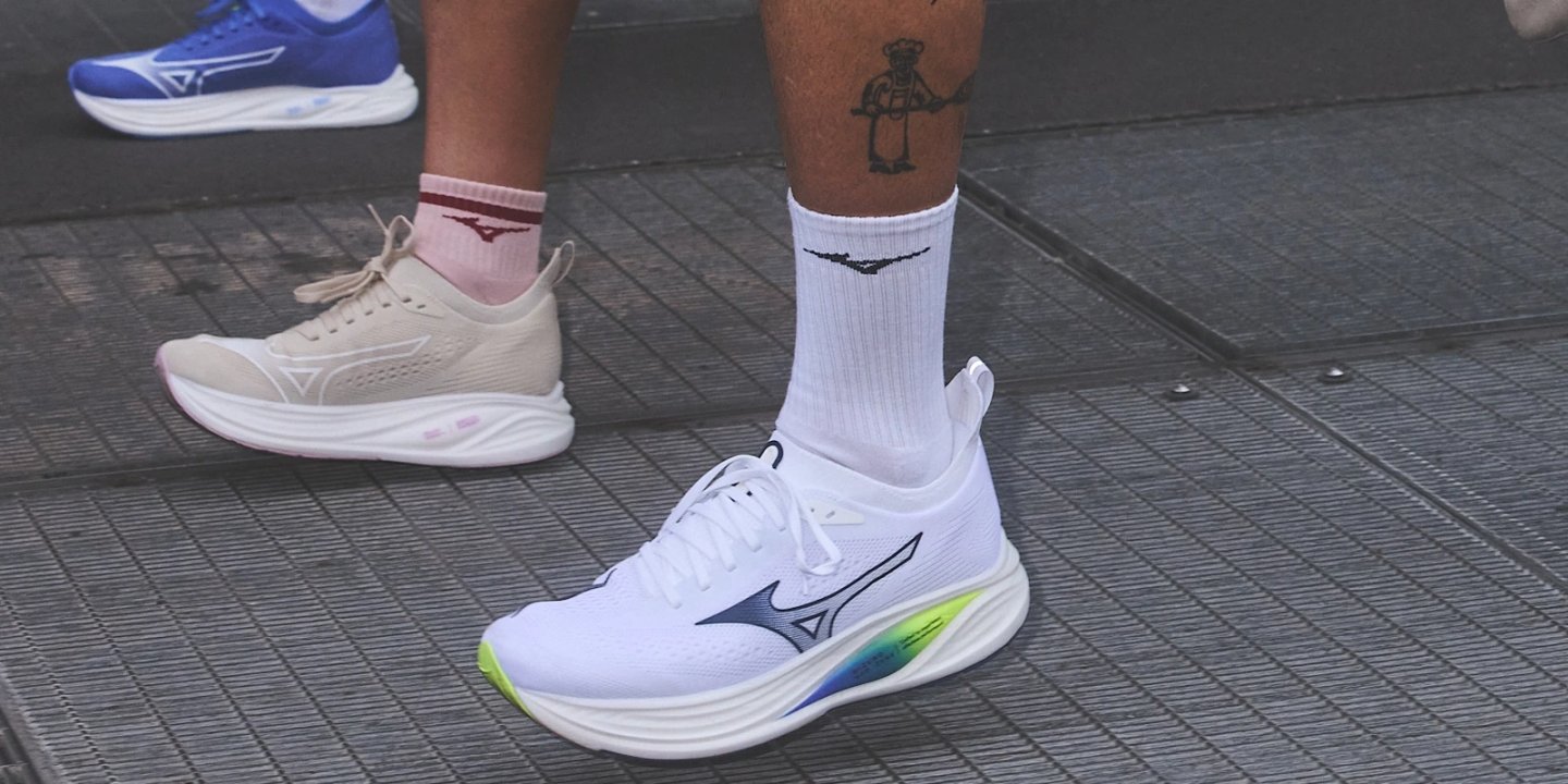 Close-up of white Mizuno running shoes with rainbow gradient midsole and navy Runbird logo, worn with white Mizuno crew socks